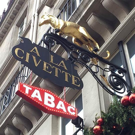 The A La Civette shop sign in Paris: a gilded civet above a black sign, with a red TABAC sign below.